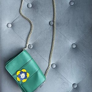 A beautiful green purse with a single flower in the front and a gold chain.